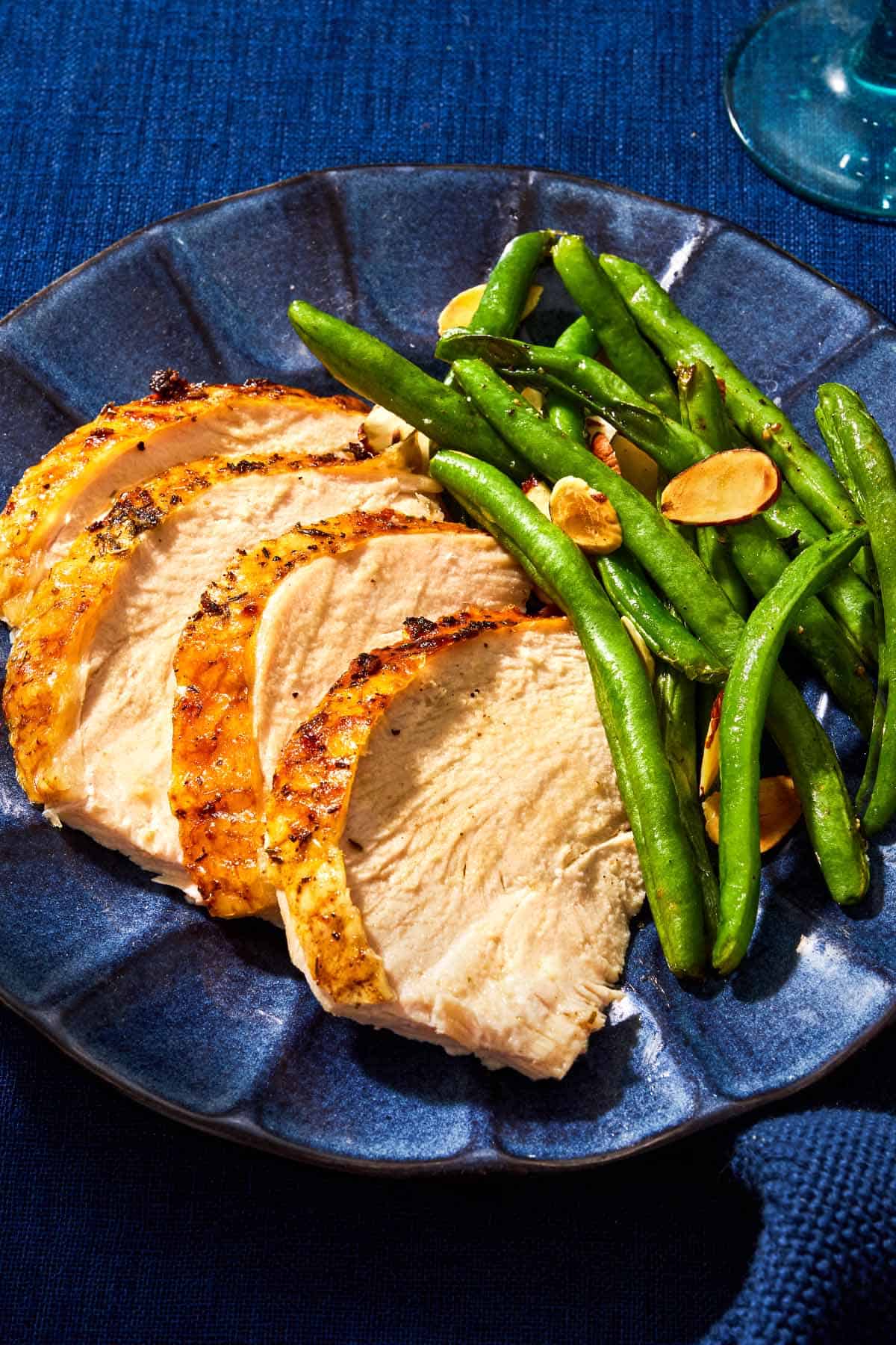 A close up of sliced roasted dry brined thanksgiving turkey on a plate with roasted green beans.