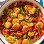 Mediterranean scallops nestled with tomatoes and bell peppers in a skillet. Next to this is a cloth napkin, a lemon, and a bowl of chopped parsley.