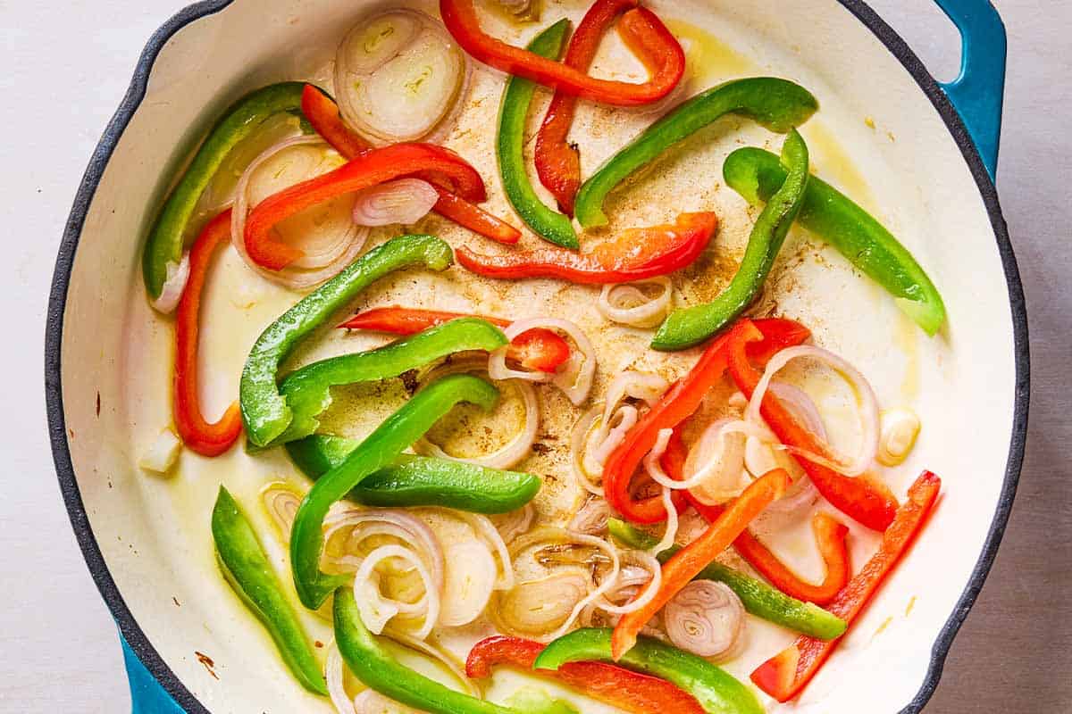 Peppers and shallots being sauteed in a skillet.