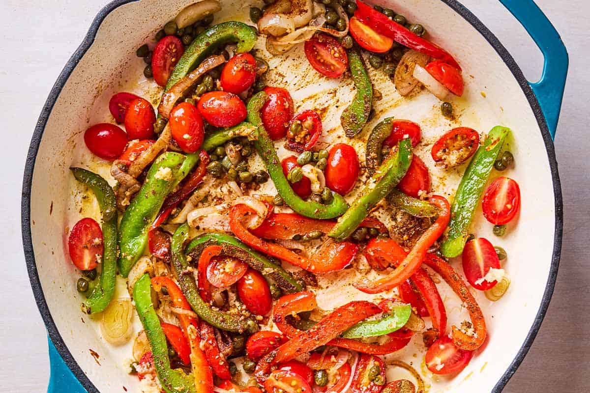 The peppers, tomatoes, shallots, capers and aromatics for the Mediterranean scallops being sauteed in a skillet.