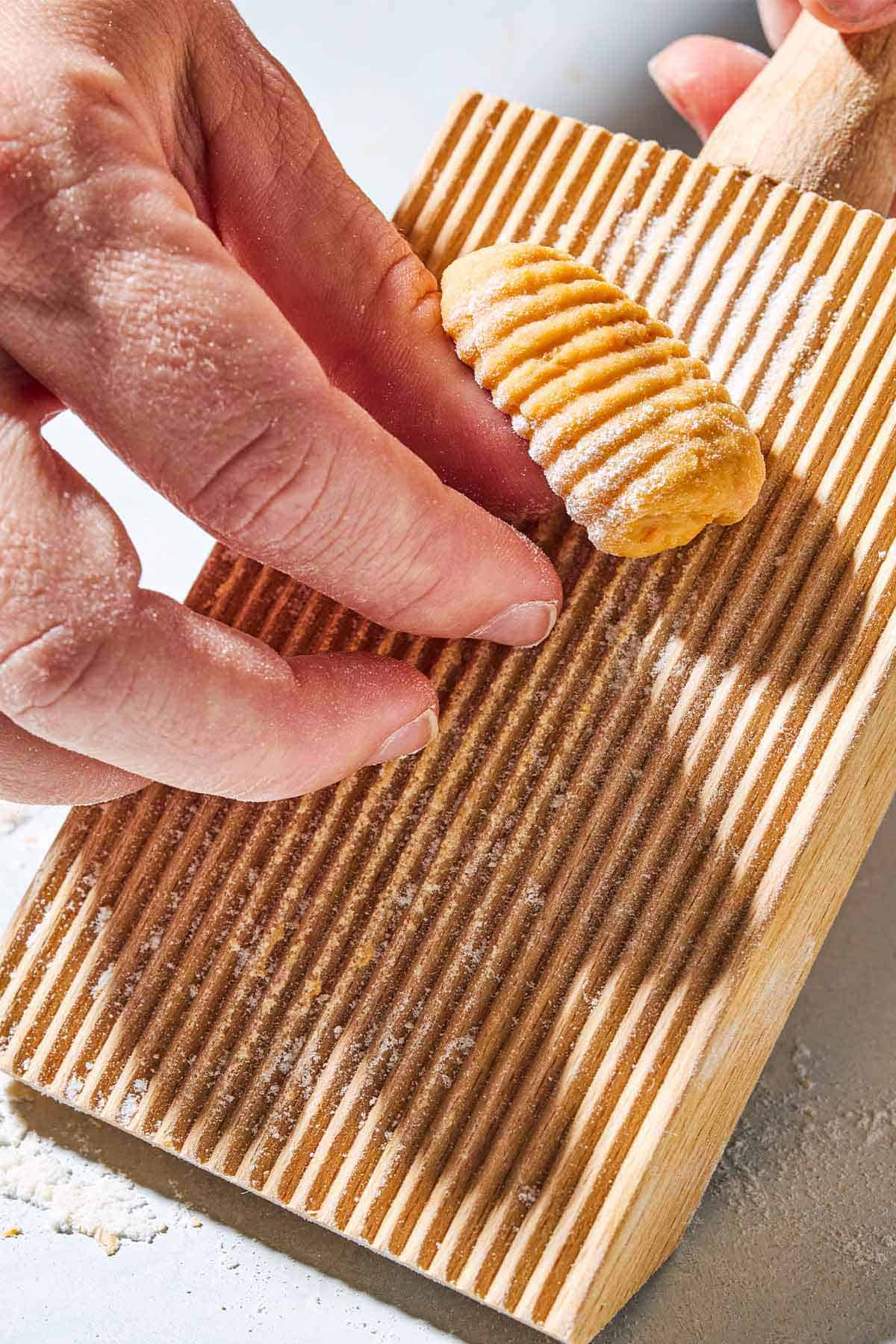 A sweet potato gnocchi being shaped on a wooden gnocchi board.