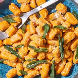 A close up of sweet potato gnocchi and sauce topped with fresh sage on a serving platter with a serving spoon spoon.