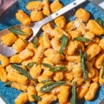 Sweet potato gnocchi and sauce topped with fresh sage on a serving platter with a serving spoon spoon.