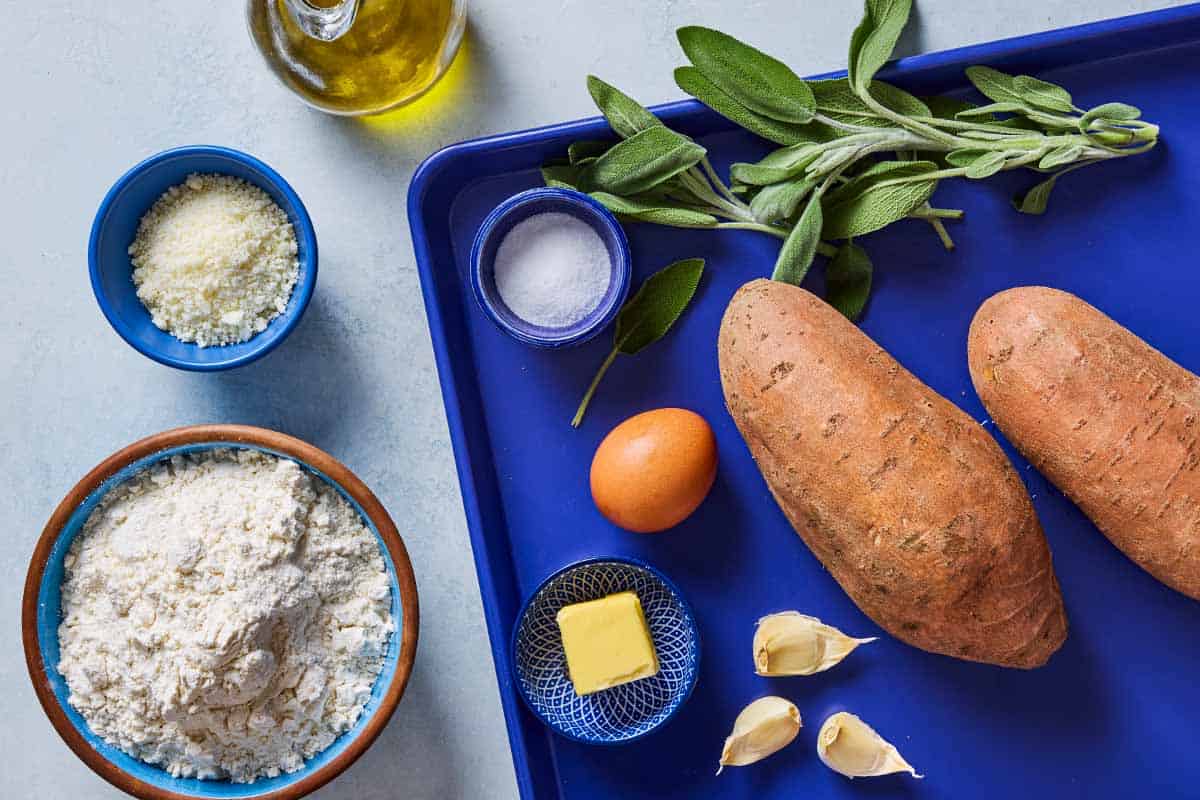 Ingredients for sweet potato gnocchi including sweet potatoes, flour, egg, salt, olive oil, butter, garlic, fresh sage, grated parmigiano- reggiano cheese.