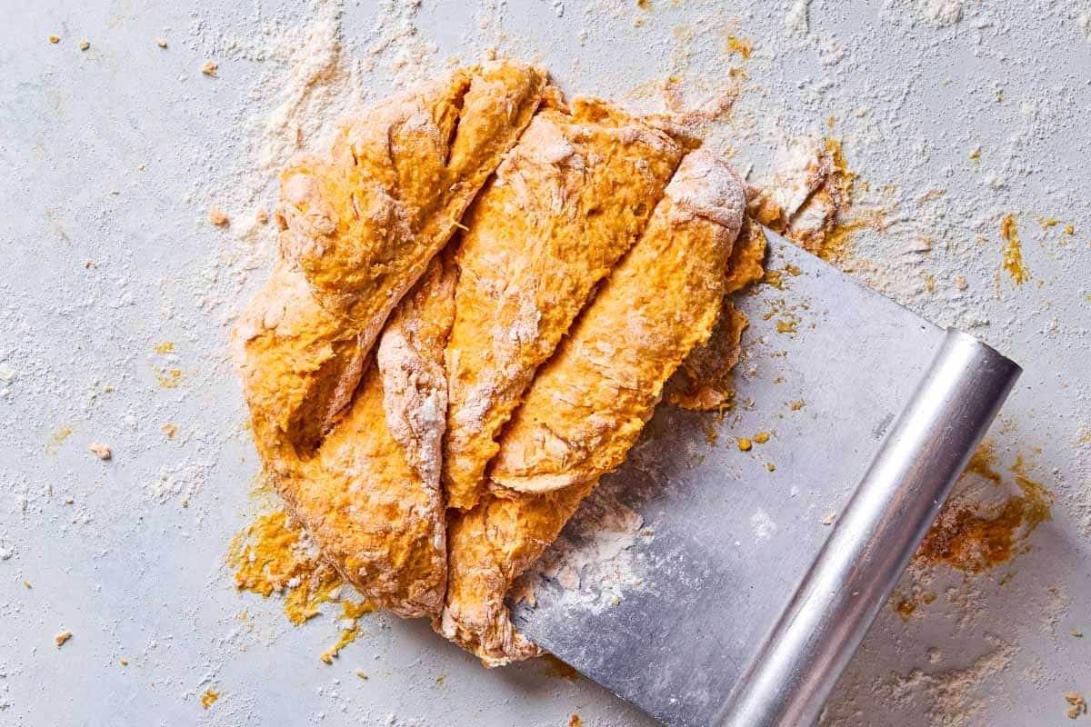 The shaggy dough for the sweet potato gnocchi being mixed together with a dough scraper.