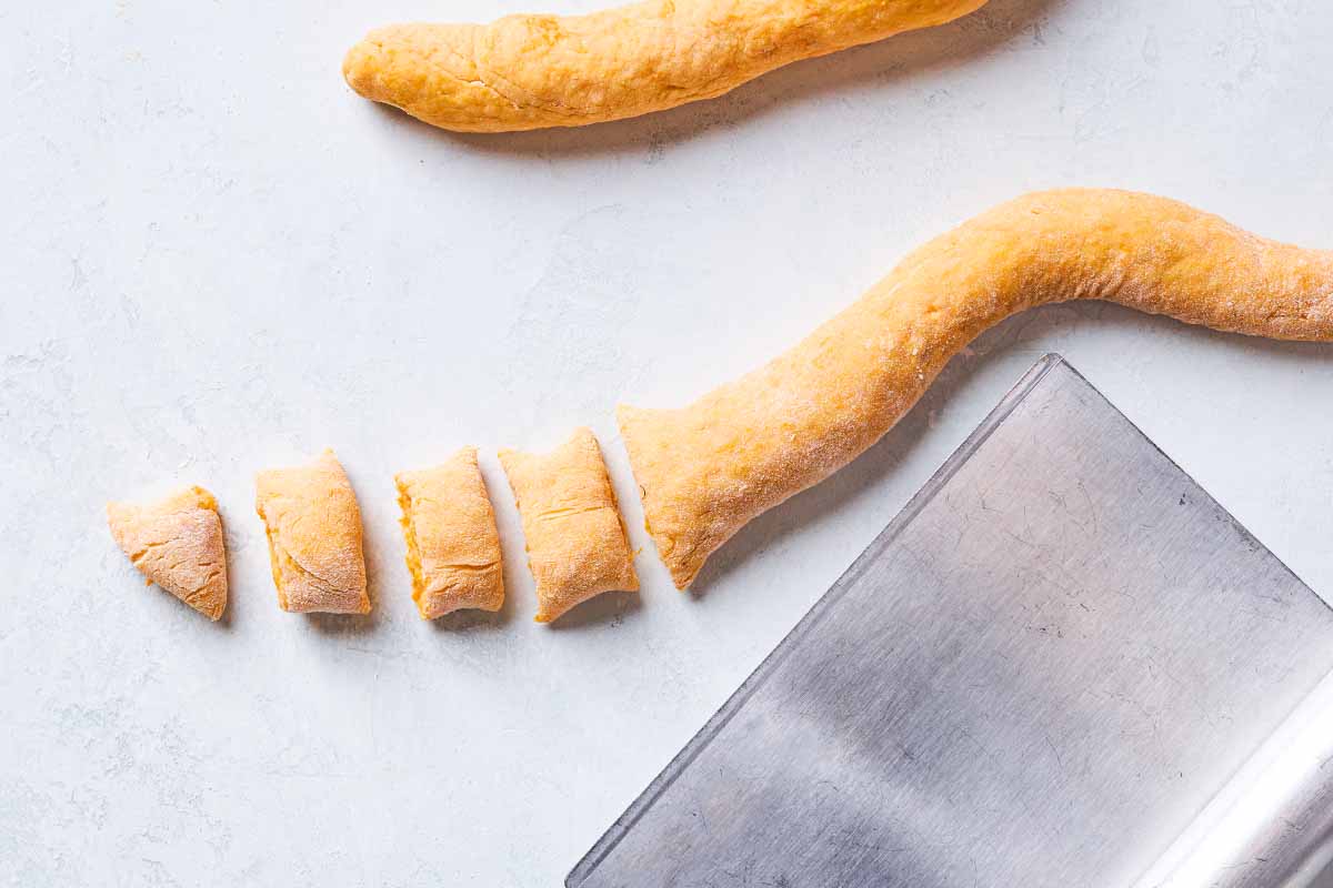 A rope of the gnocchi dough being cut into individual pieces with a dough scraper.