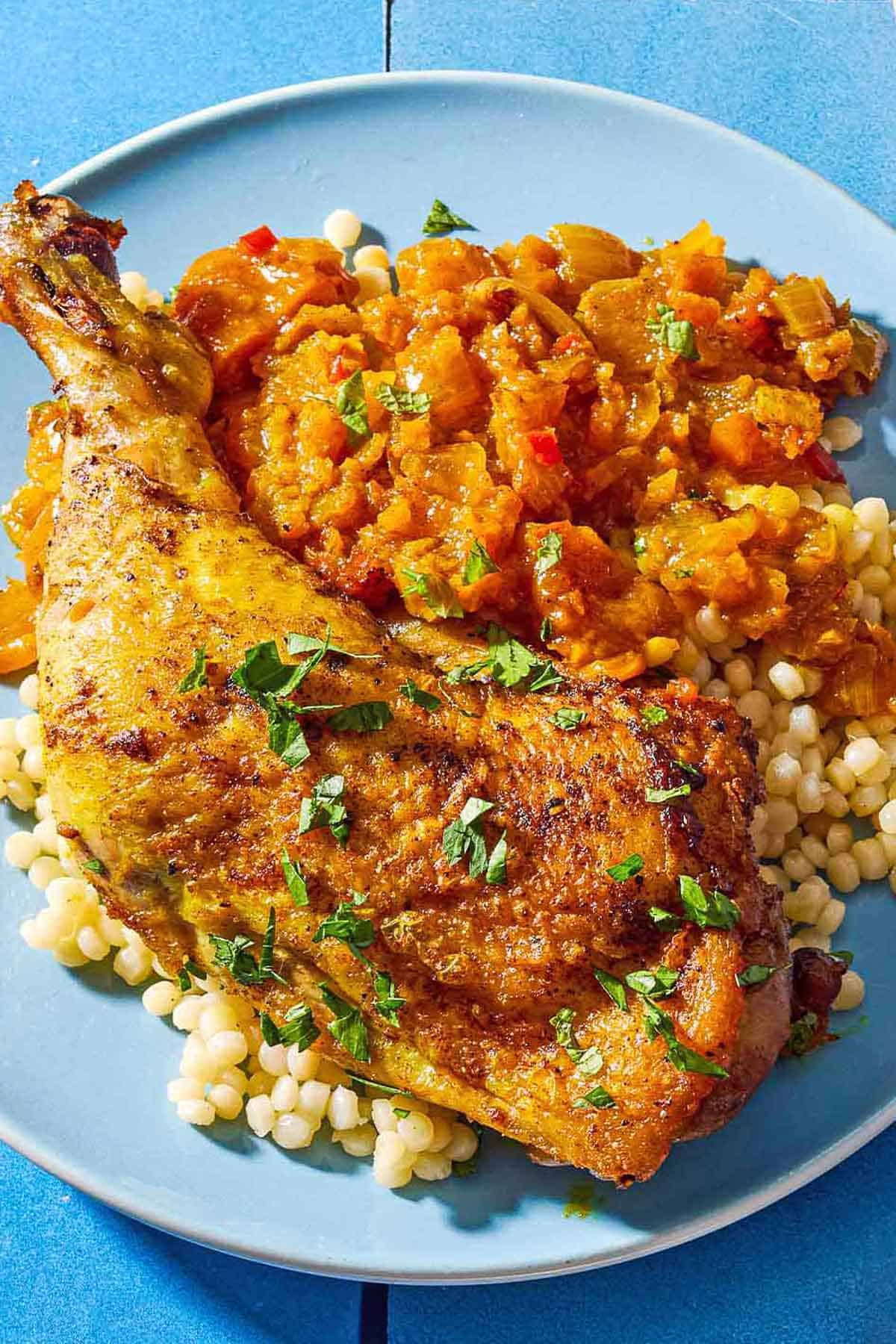 A close up of a serving of apricot chicken and apricot sauce on a bed of pearl couscous on a plate.