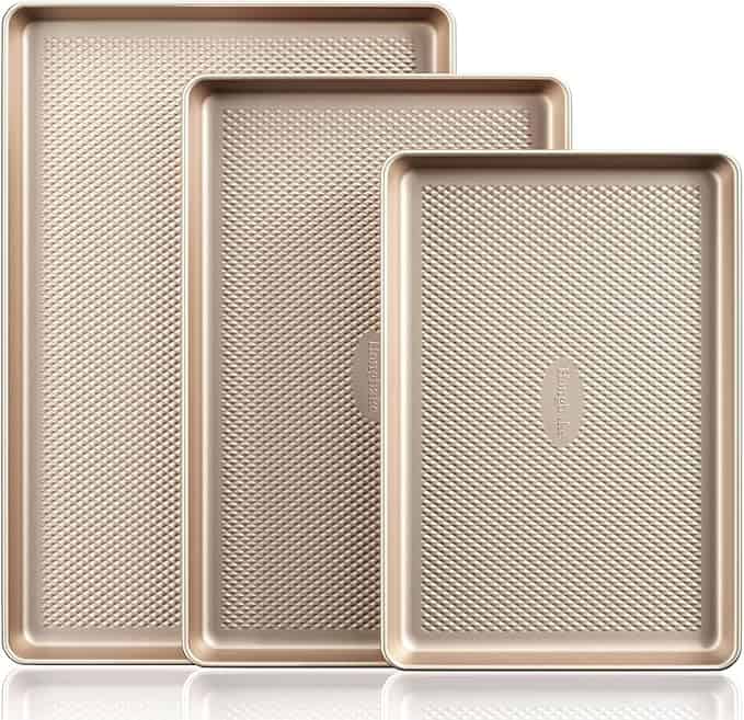 The baking sheet pan set on a white background, showing the rose gold color, diamond pattern, and three different sizes.