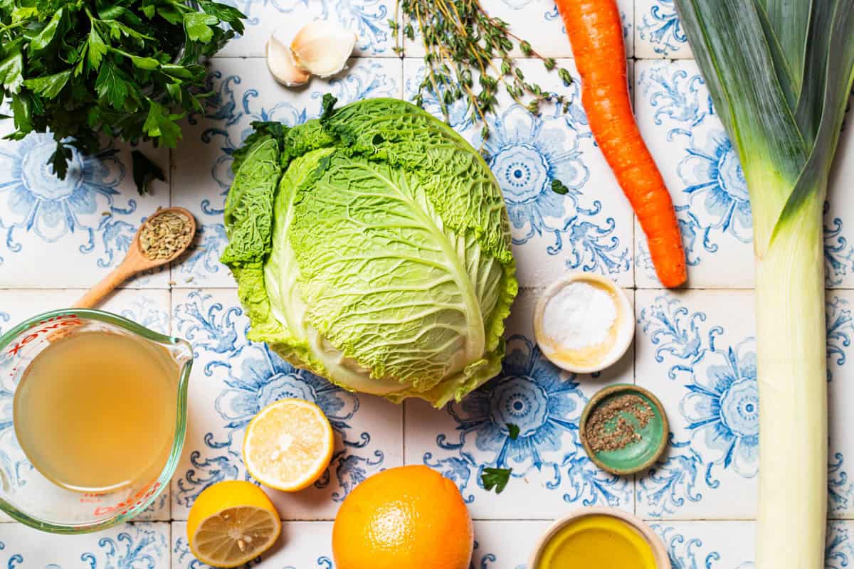 Ingredients for braised savoy cabbage including savoy cabbage, a leek, a carrot, olive oil, salt, black pepper, garlic, fennel seeds, thyme, orange, broth, lemon, and parsley.