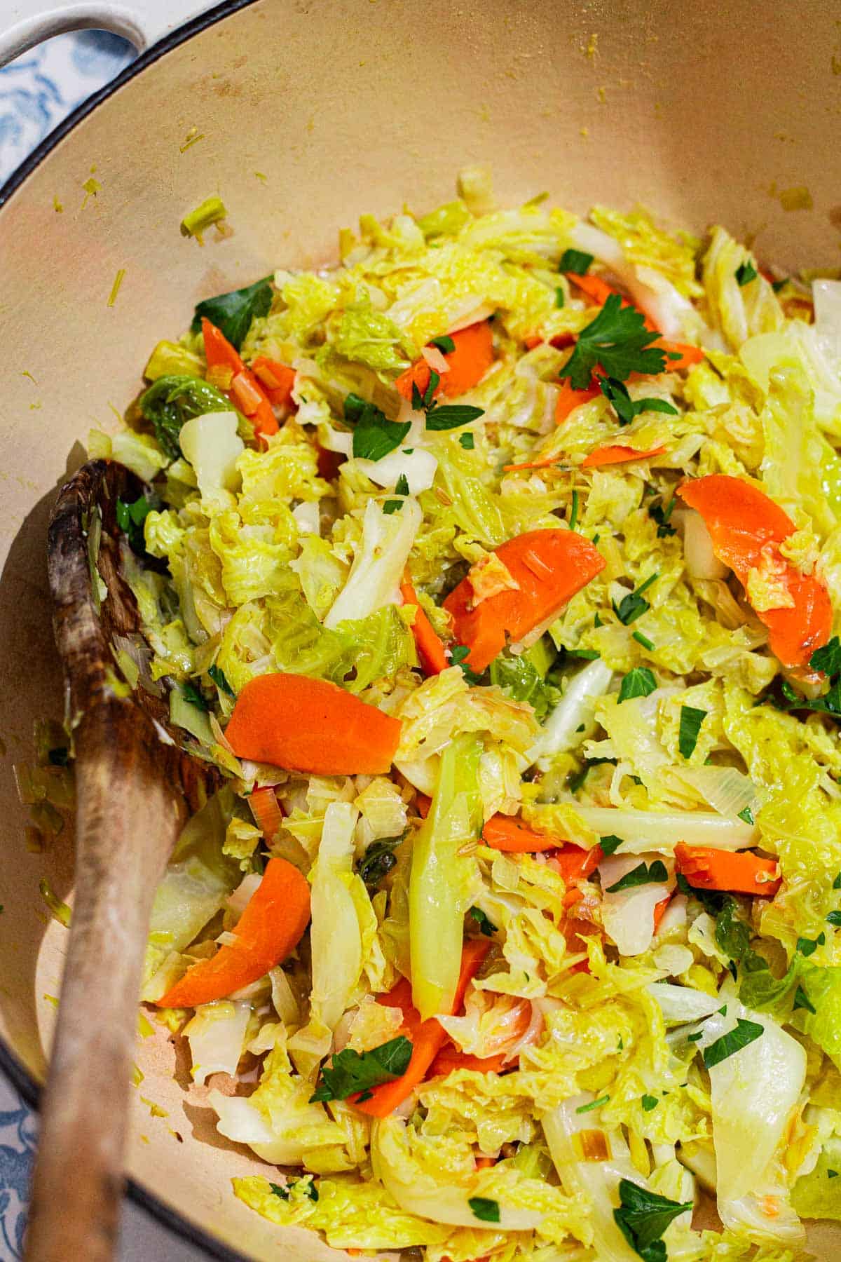 Braised savoy cabbage in a pot with a wooden spoon.