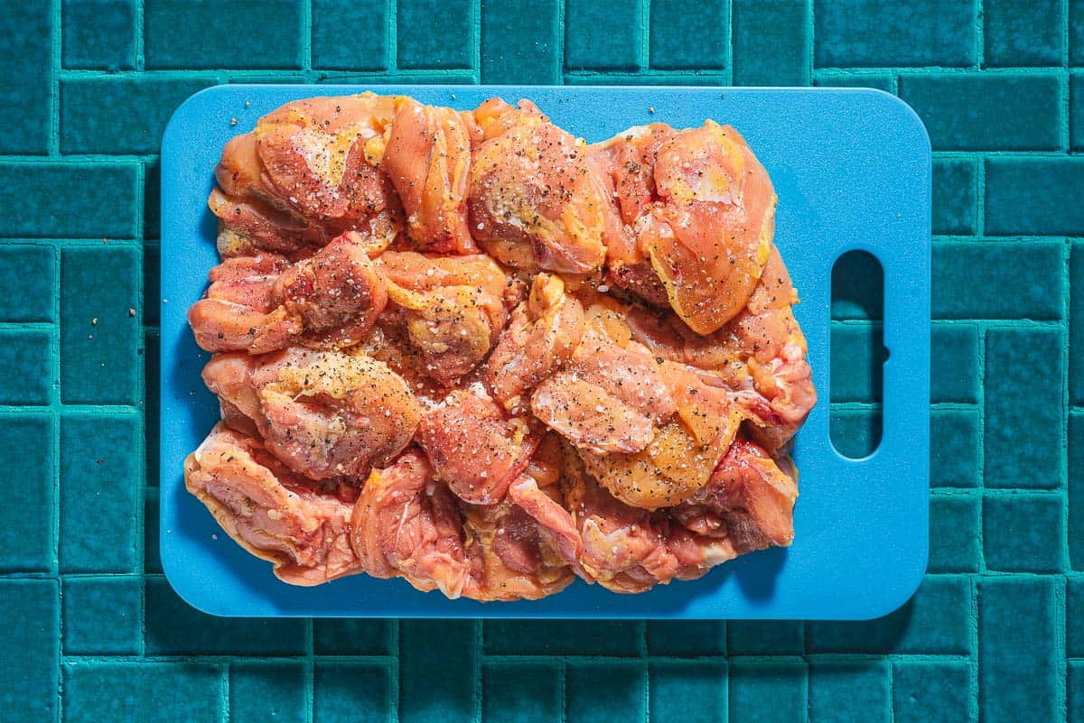 Uncooked boneless, skinless chicken thighs seasoned with salt and pepper on a cutting board.