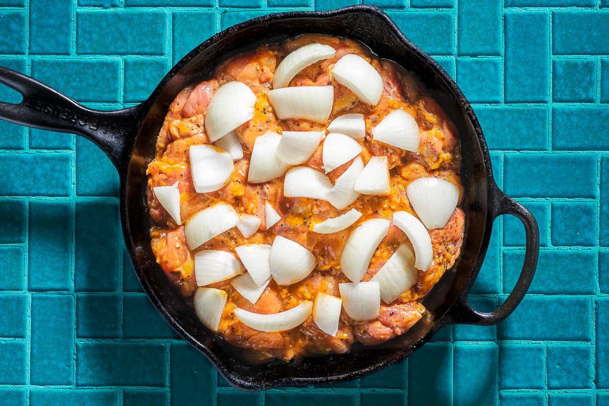 Uncooked garlic dijon chicken and onions in a cast iron skillet.