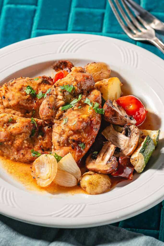 A serving of garlic dijon chicken with roasted vegetable on a plate. Next to this is a cloth napkin, fork and knife.