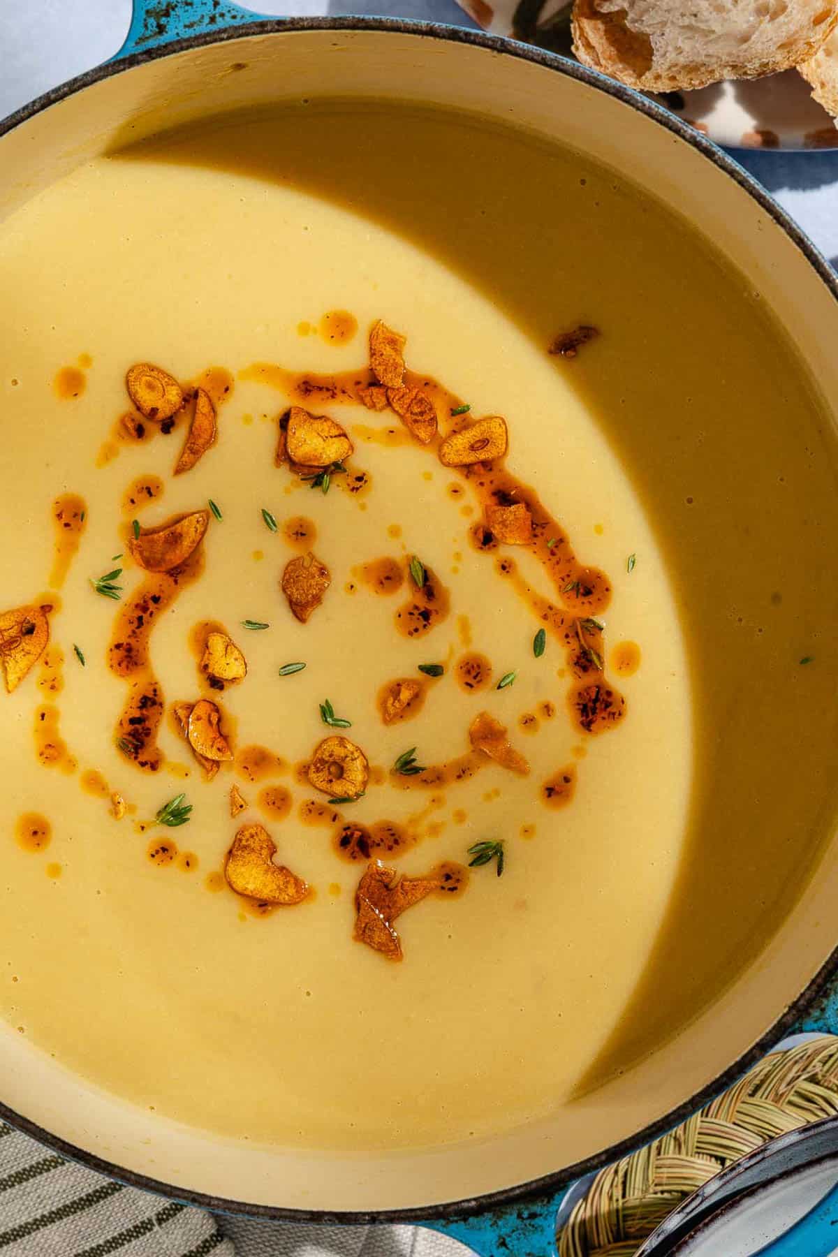 An overhead photo of garlic soup topped with fried garlic and aleppo oil in a large pot.