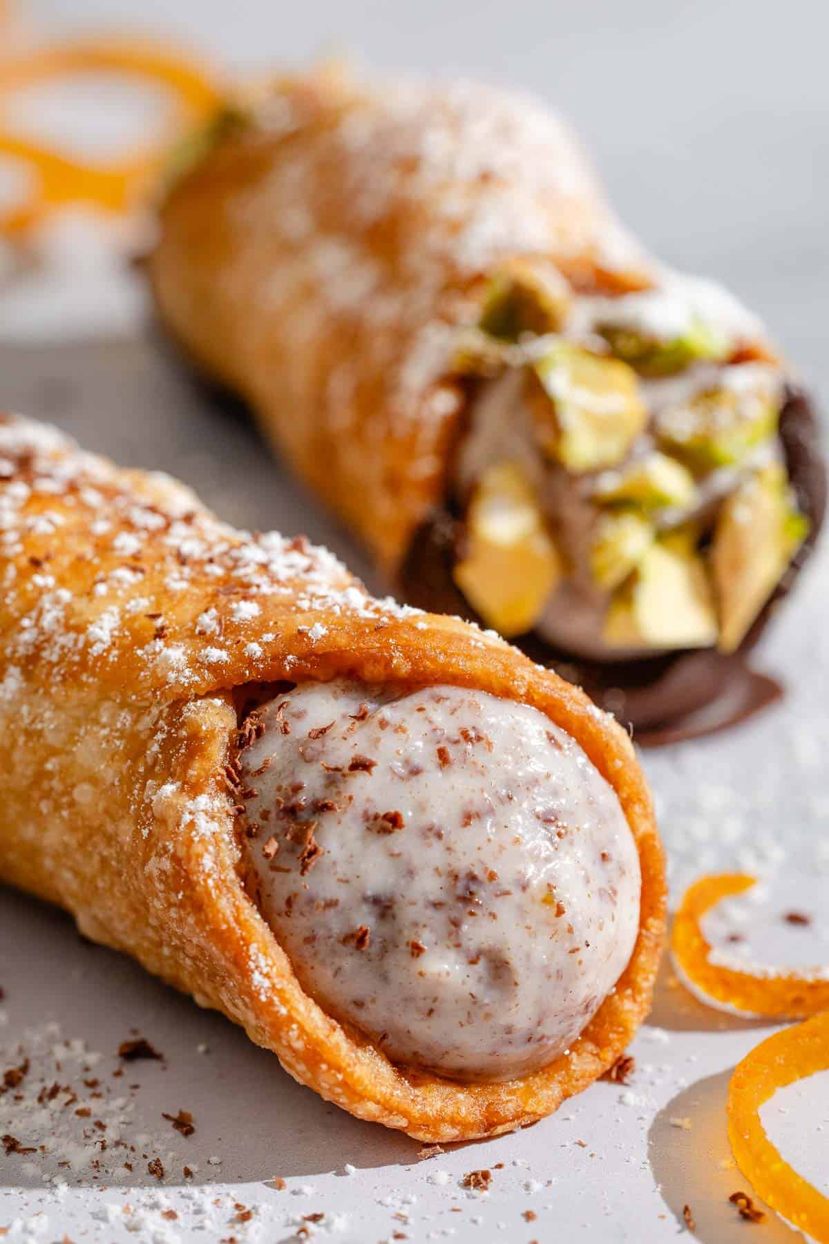 A close up of a filled cannoli with another in the background.