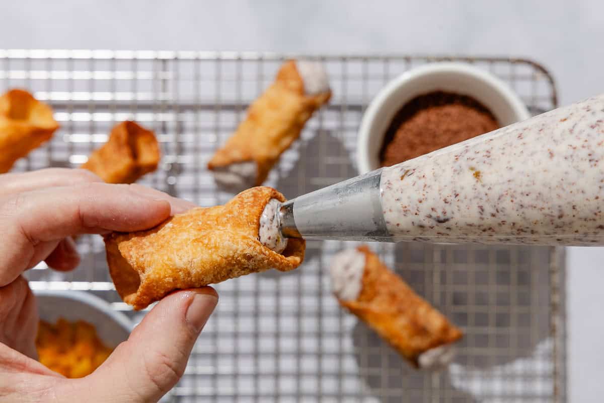 A close up of a cannoli shell being filled with the filling.