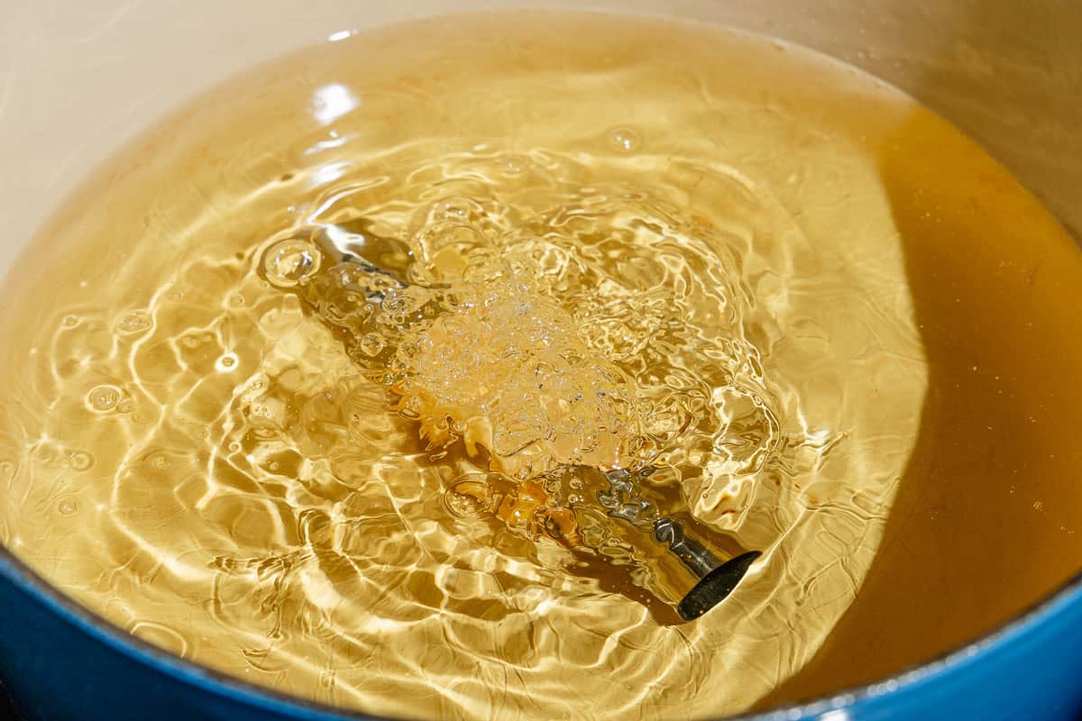 A cannoli shell wrapped around a cannoli mold in a pot of hot oil.