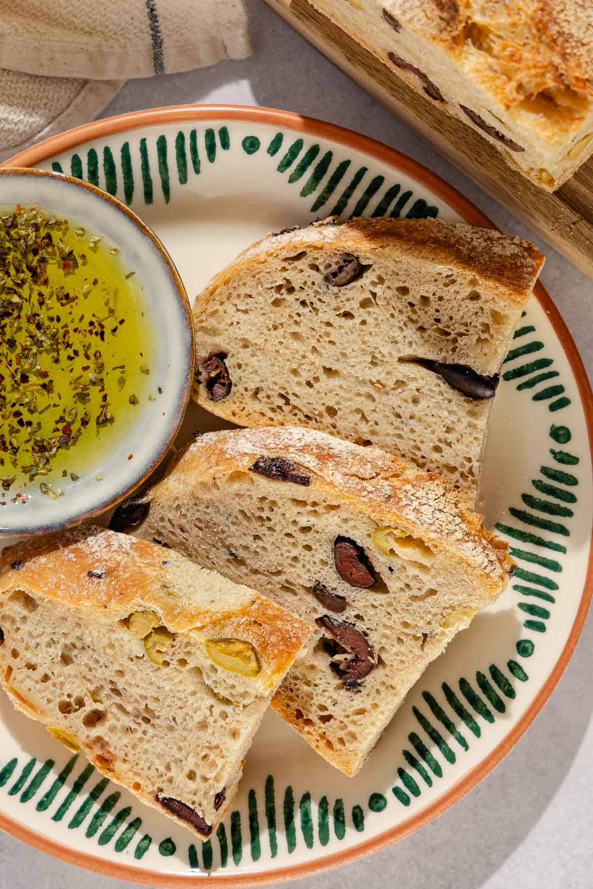 A close up of 3 slices of olive bread on a plate with a small bowl of olive oil.