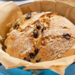 A close up of a baked loaf of olive bread in a parchment lined dutch oven.