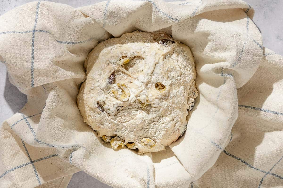 An overhead photo of the ball of olive oil dough in a towel-lined bowl.