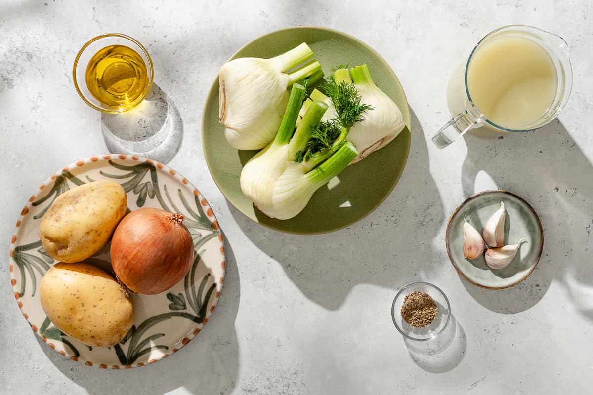 Ingredients for fennel soup including stock, onion, fennel bulbs, fennel seeds, garlic, gold potatoes, kosher salt and black pepper.