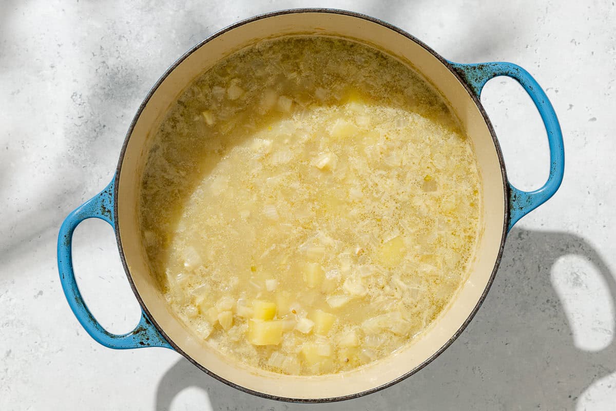 An overhead photo of diced potatoes, onion and fennel simmering s stock in a large pot.