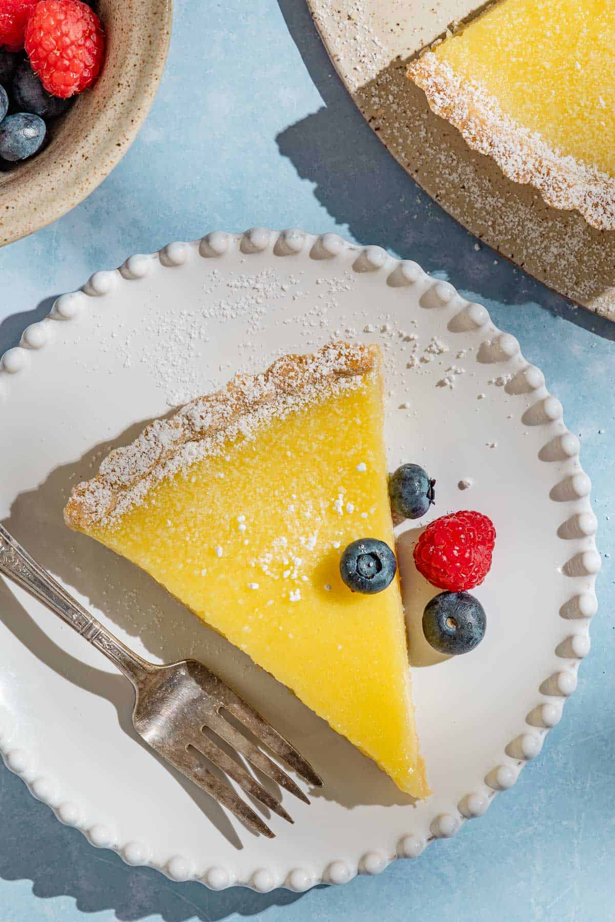 An overhead photo of a slice of the lemon tart on a plate with a fork and some berries.