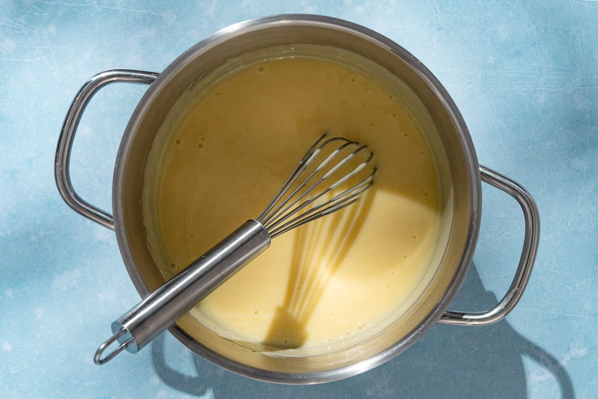 An overhead photo of the filling for the lemon curd tart cooking in a large pot with a whisk.