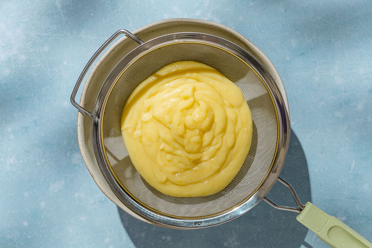 On overhead photo of the filling for the lemon tart in a strainer sitting on a large bowl.