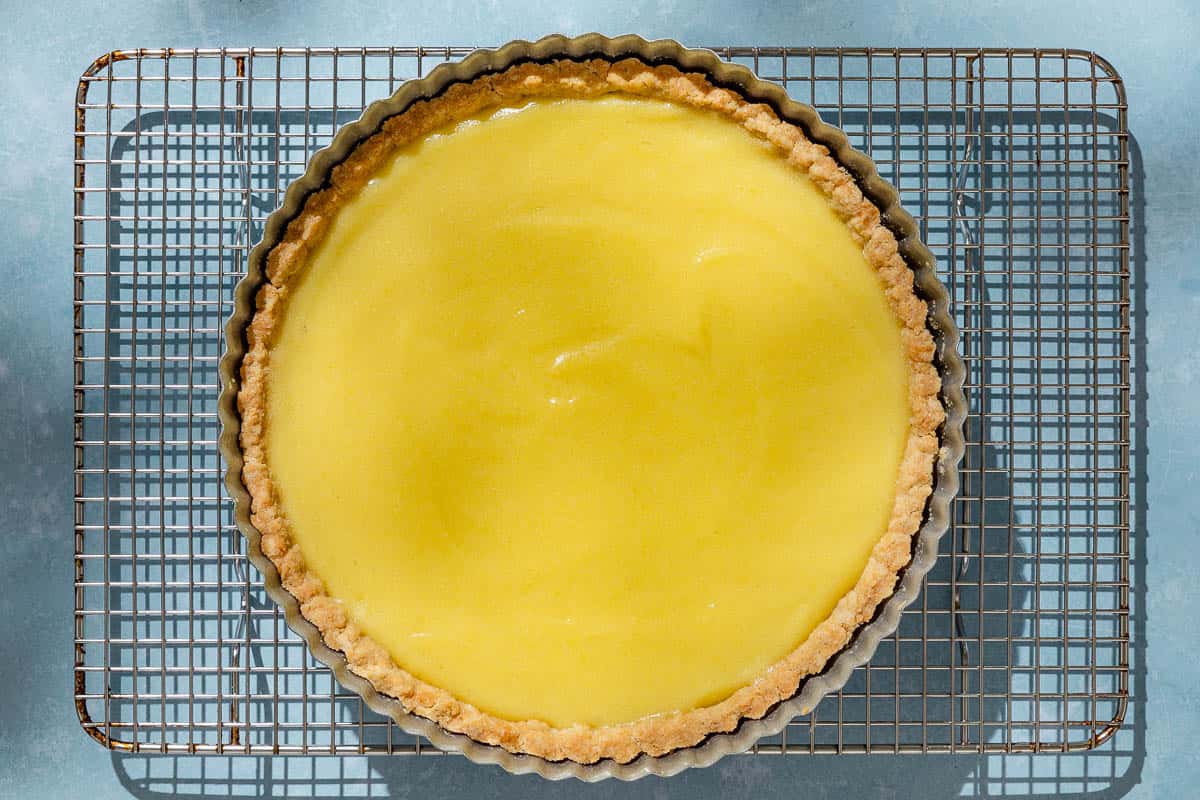 An overhead photo of a baked lemon tart in a tart pan cooling on a wire rack.