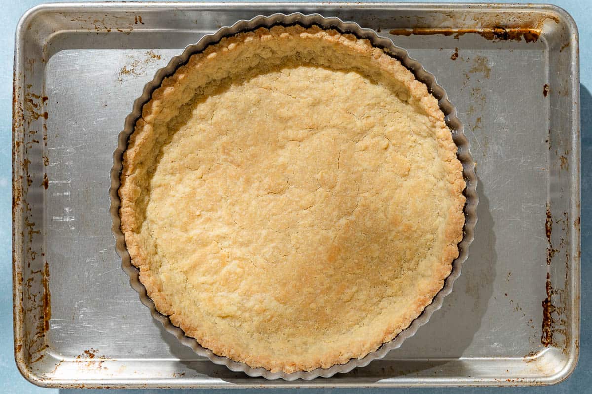 An overhead photo of a baked crust in a tart pan on a baking sheet.