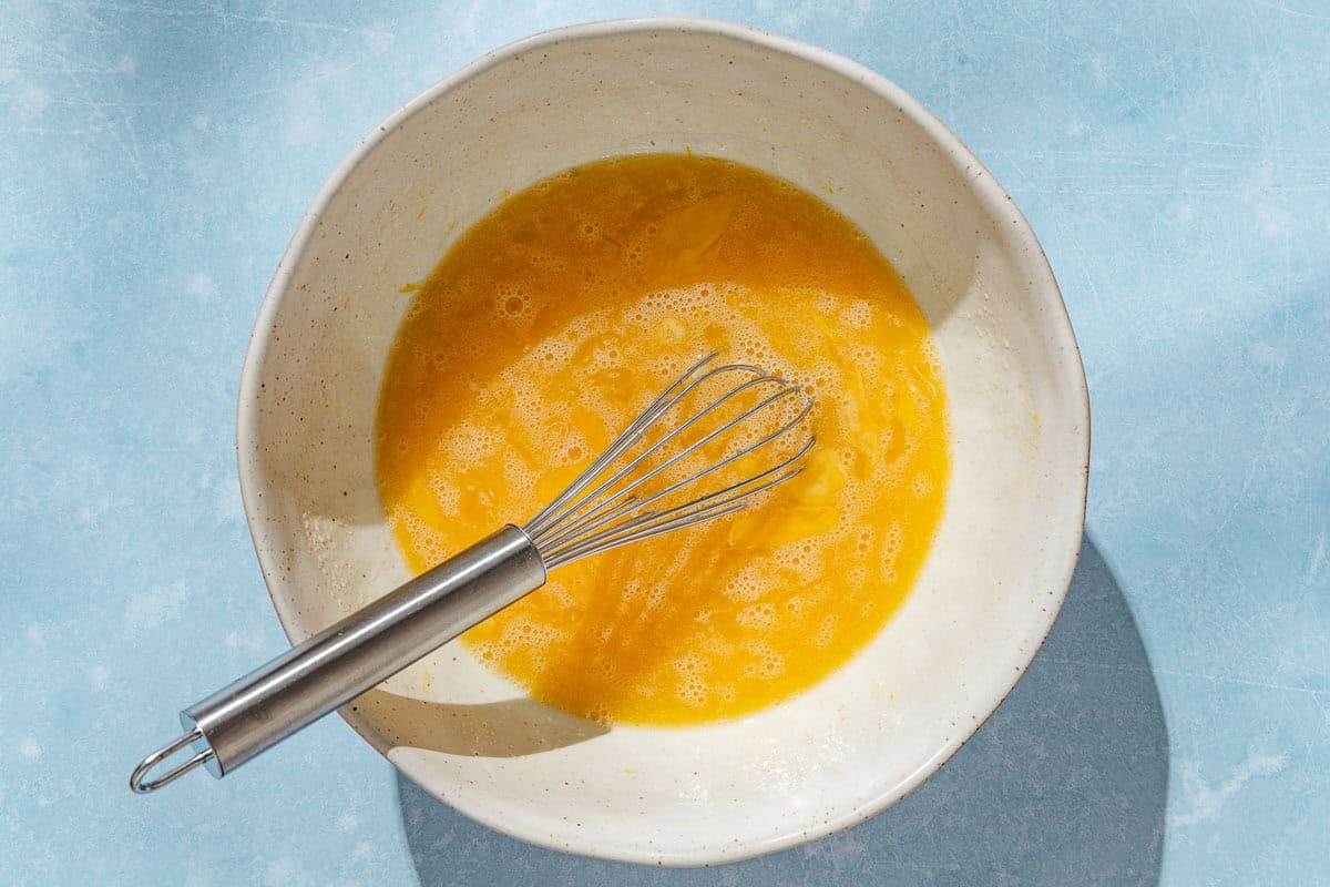 An overhead photo of eggs beaten together in a bowl with a whisk.