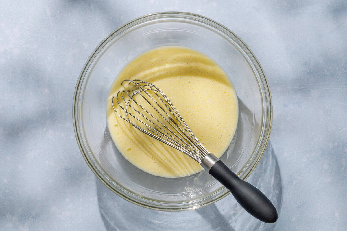 An overhead photo of the wet ingredients for the pistachio cake mixed together in a bowl with a whisk.