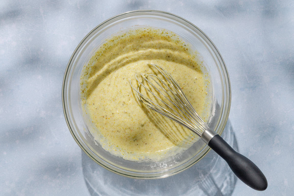 An overhead photo of the batter for the pistachio cake mixed together in a bowl with a whisk.