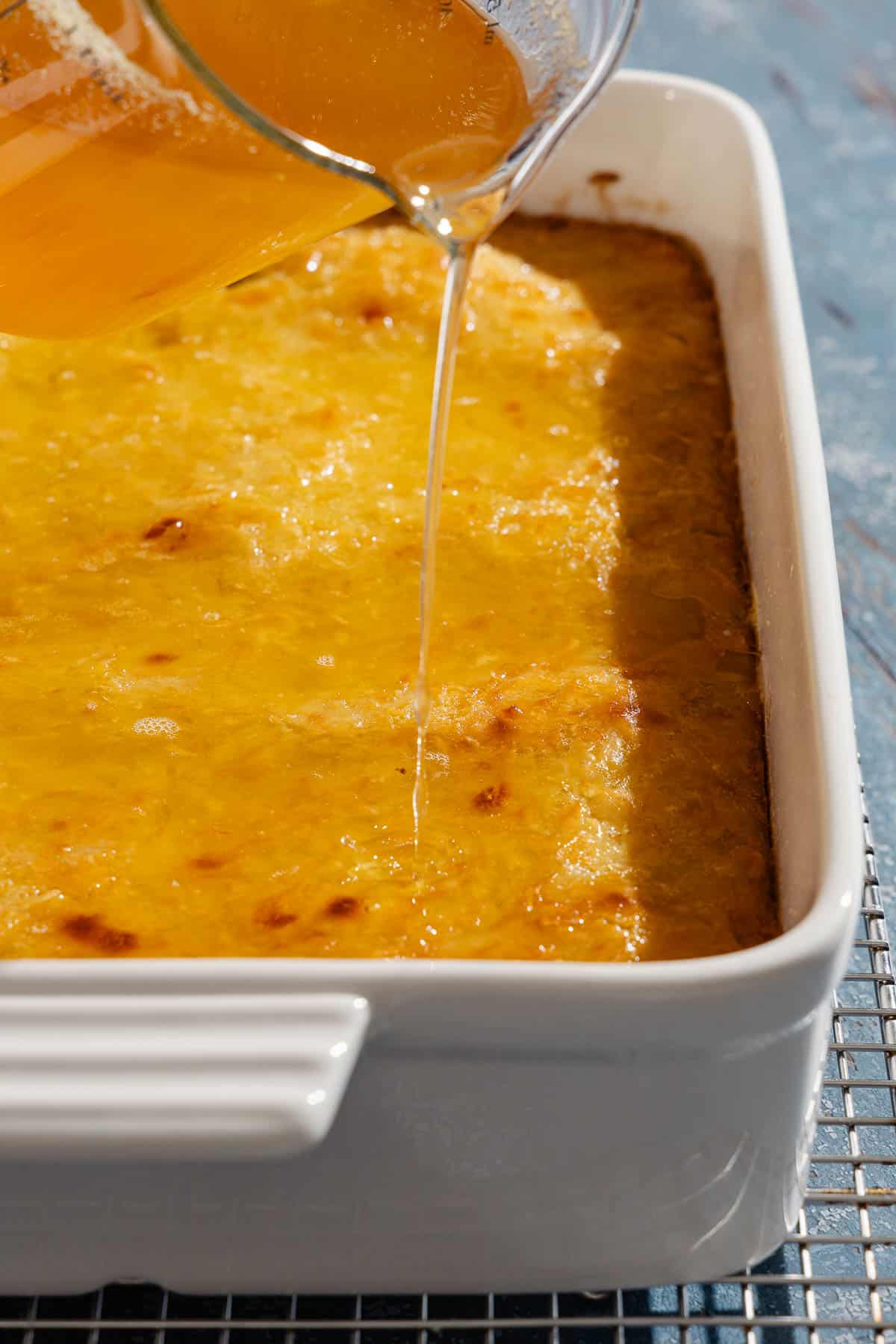 A close up of the honey orange syrup being poured on portokalopita greek orange cake in a baking dish.