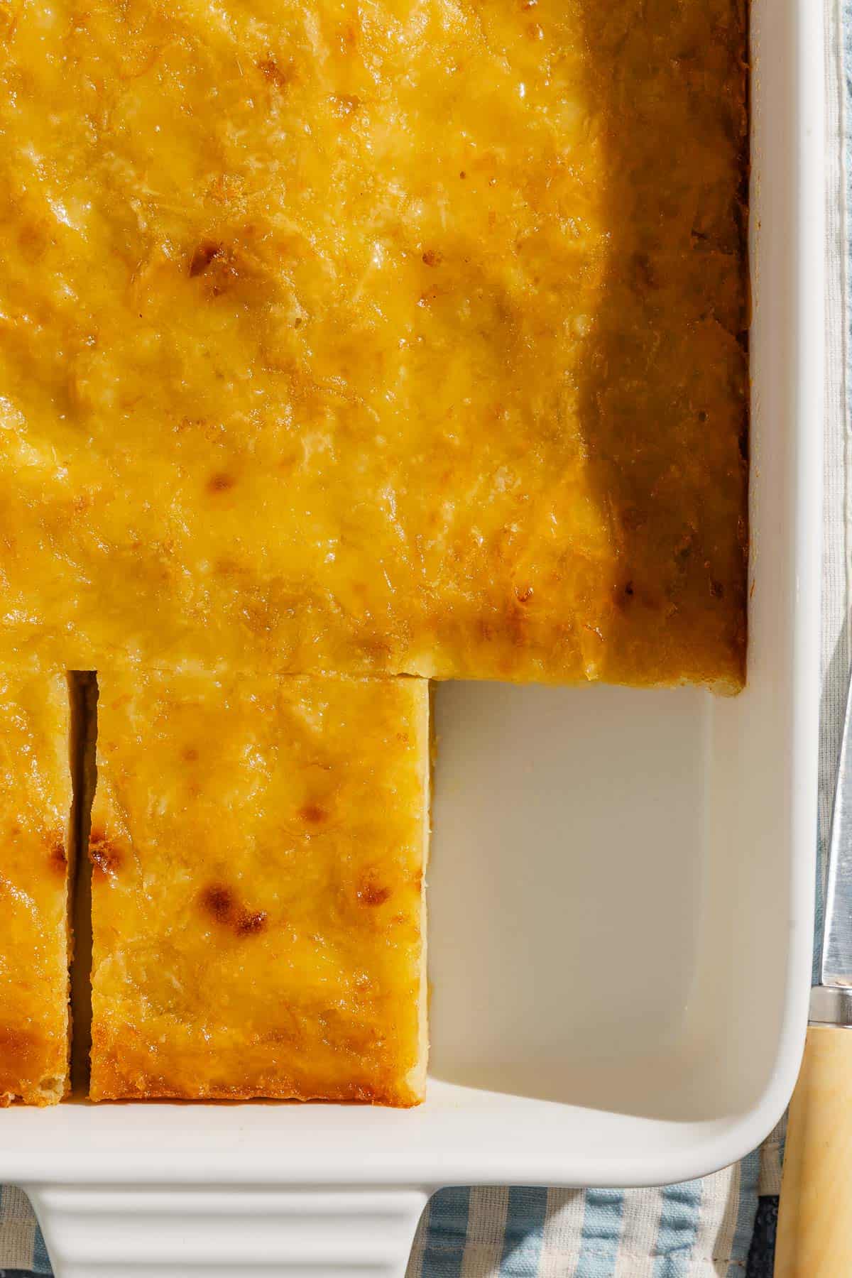 A close up of portokalopita greek orange cake in a baking dish with one piece missing.