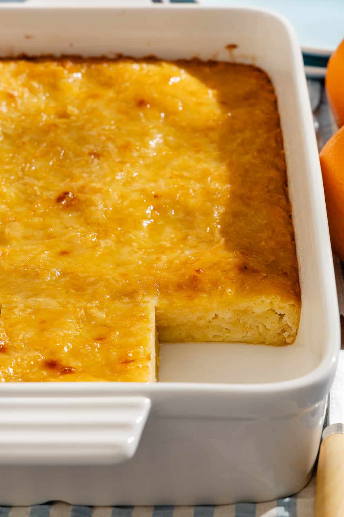 A close up of portokalopita greek orange cake in a baking dish with one piece missing.