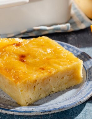 A close up of a piece of portokalopita greek orange cake on a plate next to another plate with orange wedges.