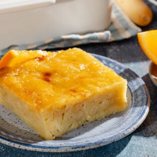 A close up of a piece of portokalopita greek orange cake on a plate next to another plate with orange wedges.