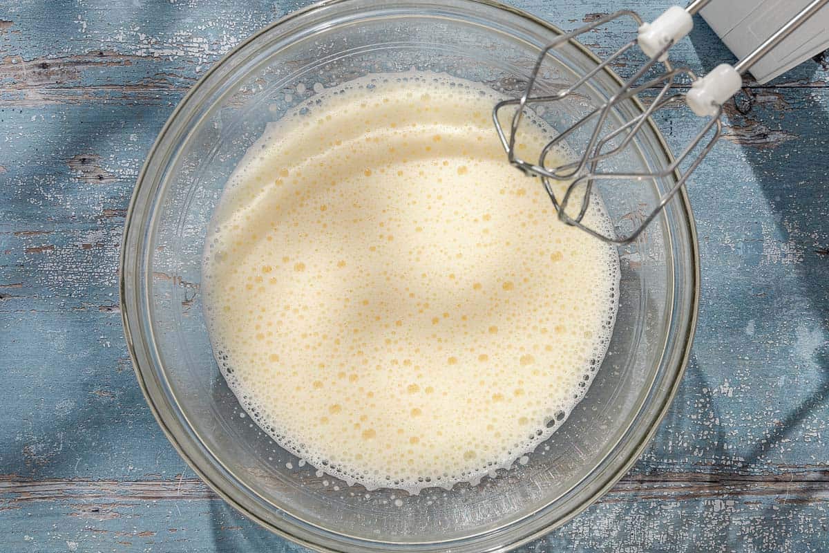 An overhead photo of eggs and sugar in a bowl after being mixed together. Next to this is a hand mixer.