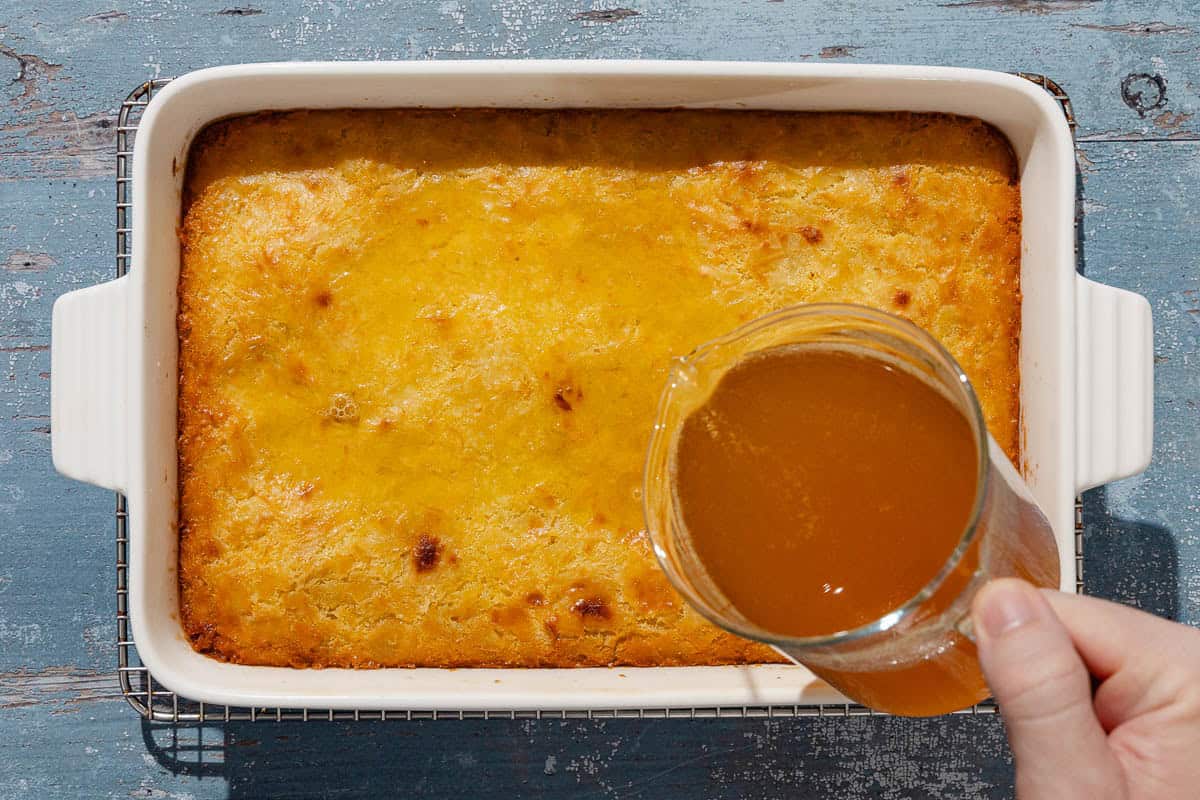 An overhead photo of the honey orange syrup being poured on portokalopita greek orange cake in a baking dish.