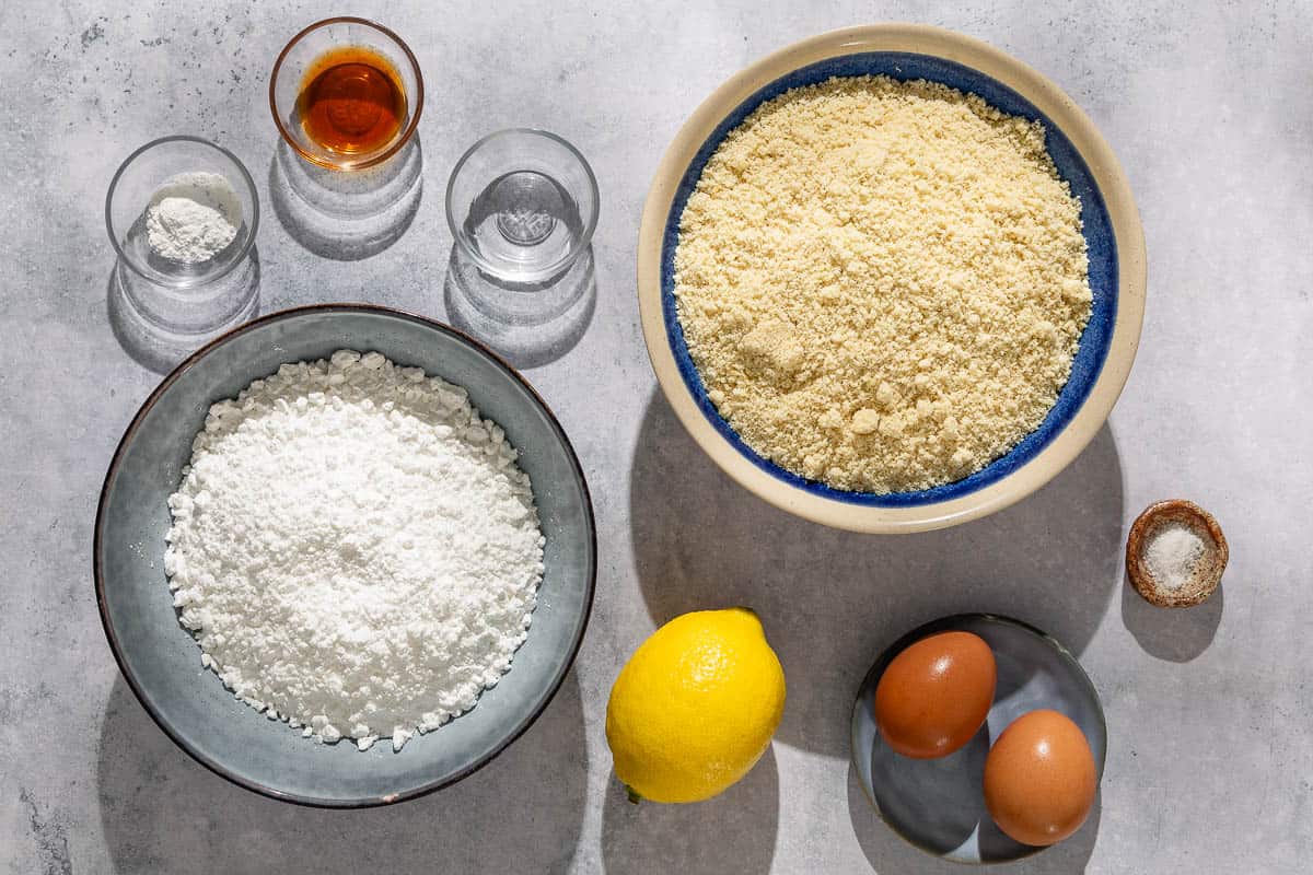 Ingredients for ricciarelli cookies including almond flour, powdered sugar, baking powder, salt, eggs, vanilla extract, almond extract and lemon.