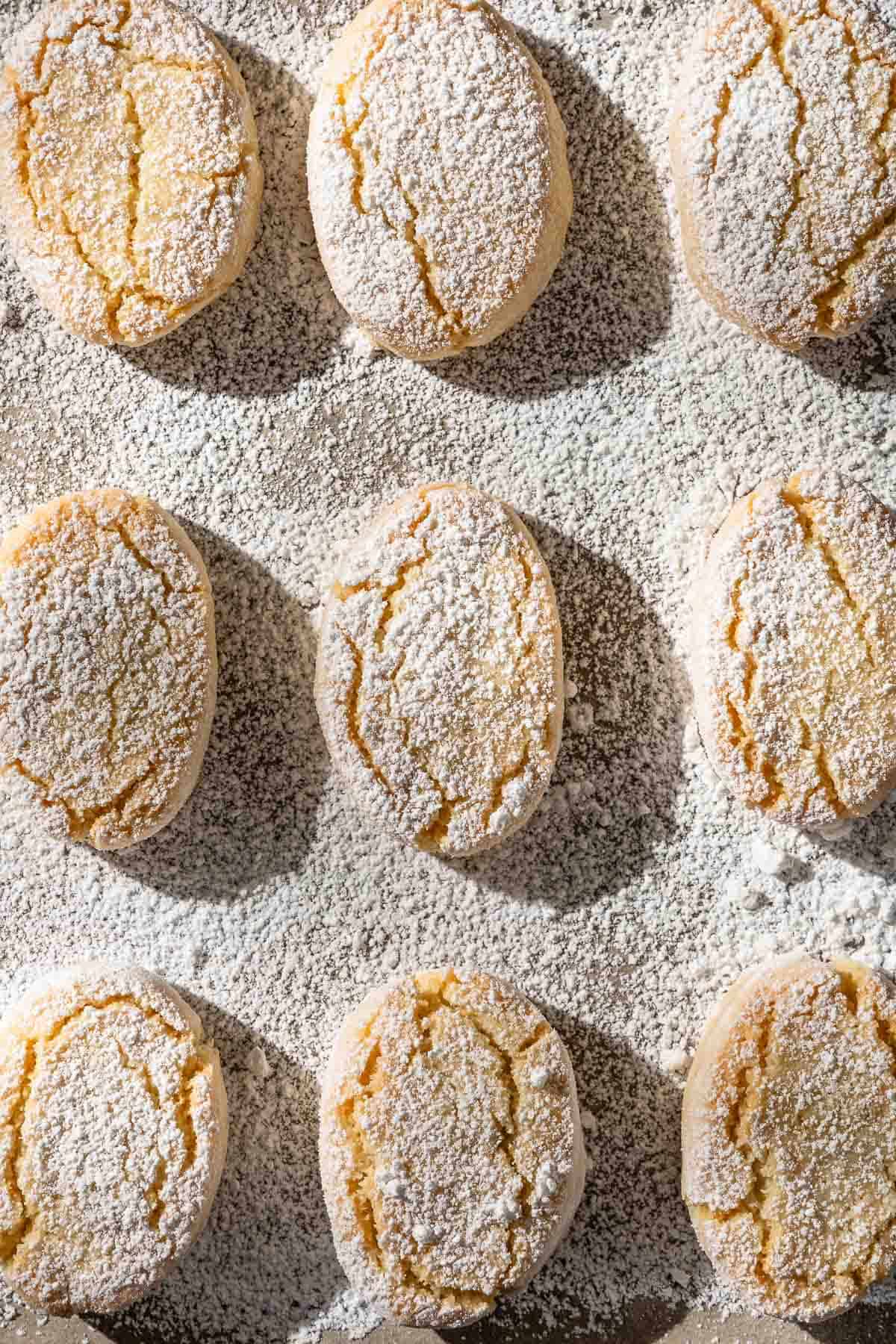 A close up of baked ricciarelli cookies topped with powdered sugar on a parchment line sheet pan.