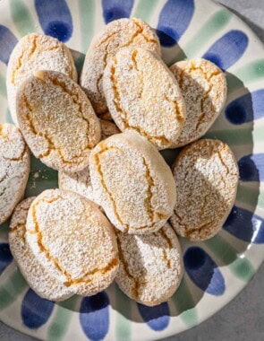 Baked ricciarelli cookies topped with powdered sugar on a plate.