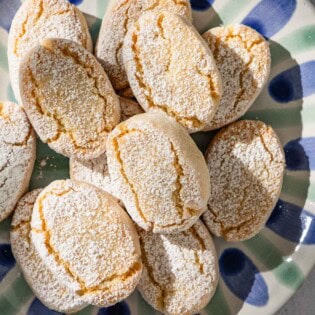 Baked ricciarelli cookies topped with powdered sugar on a plate.