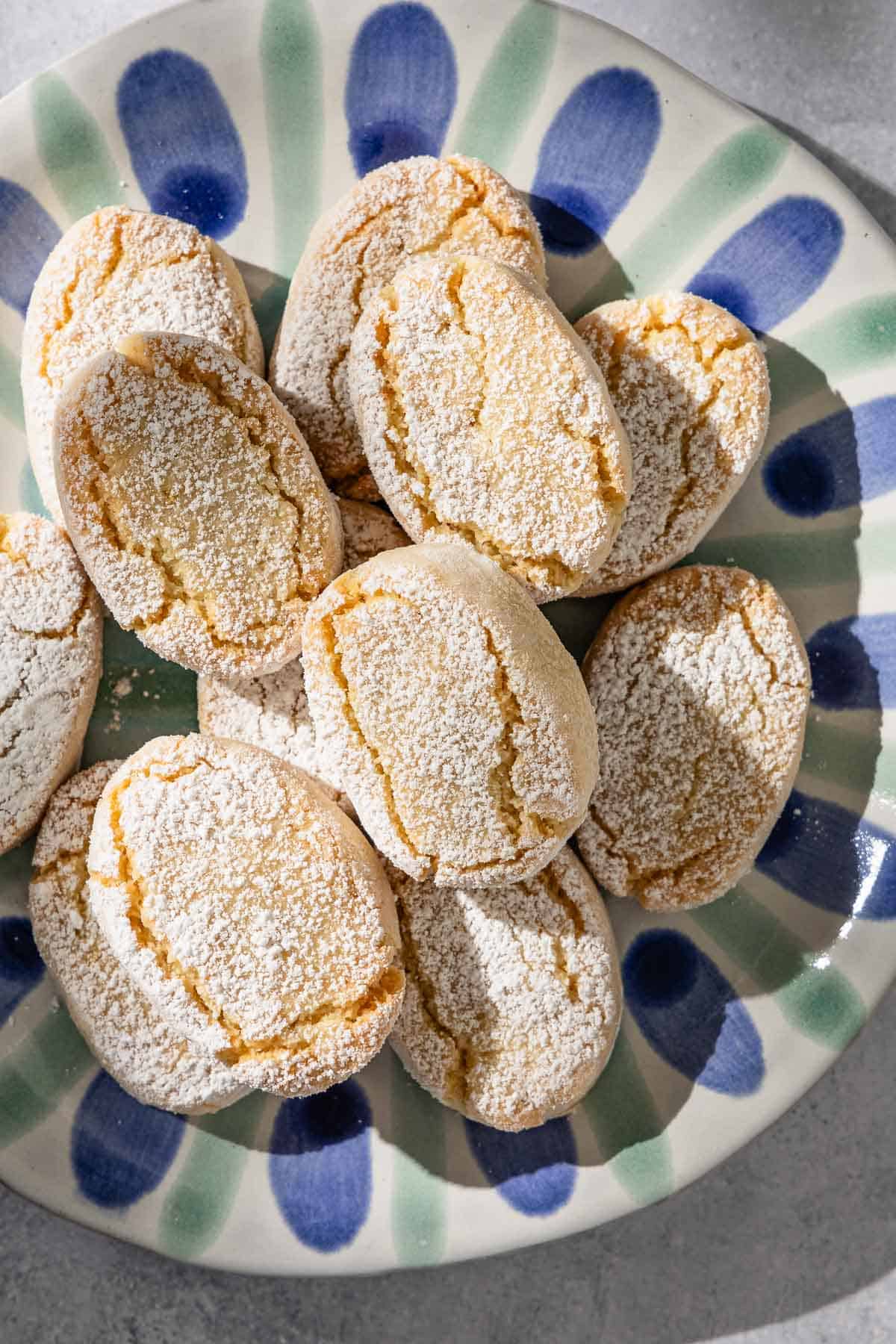 Baked ricciarelli cookies topped with powdered sugar on a plate.