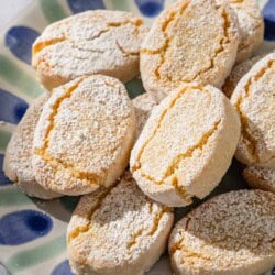 A close up of baked ricciarelli cookies topped with powdered sugar on a plate.