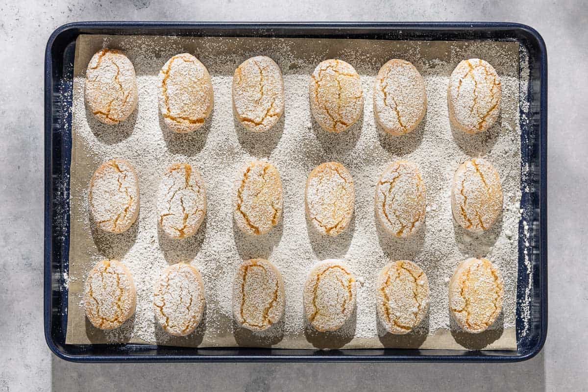 Baked ricciarelli cookies topped with powdered sugar on a parchment line sheet pan.