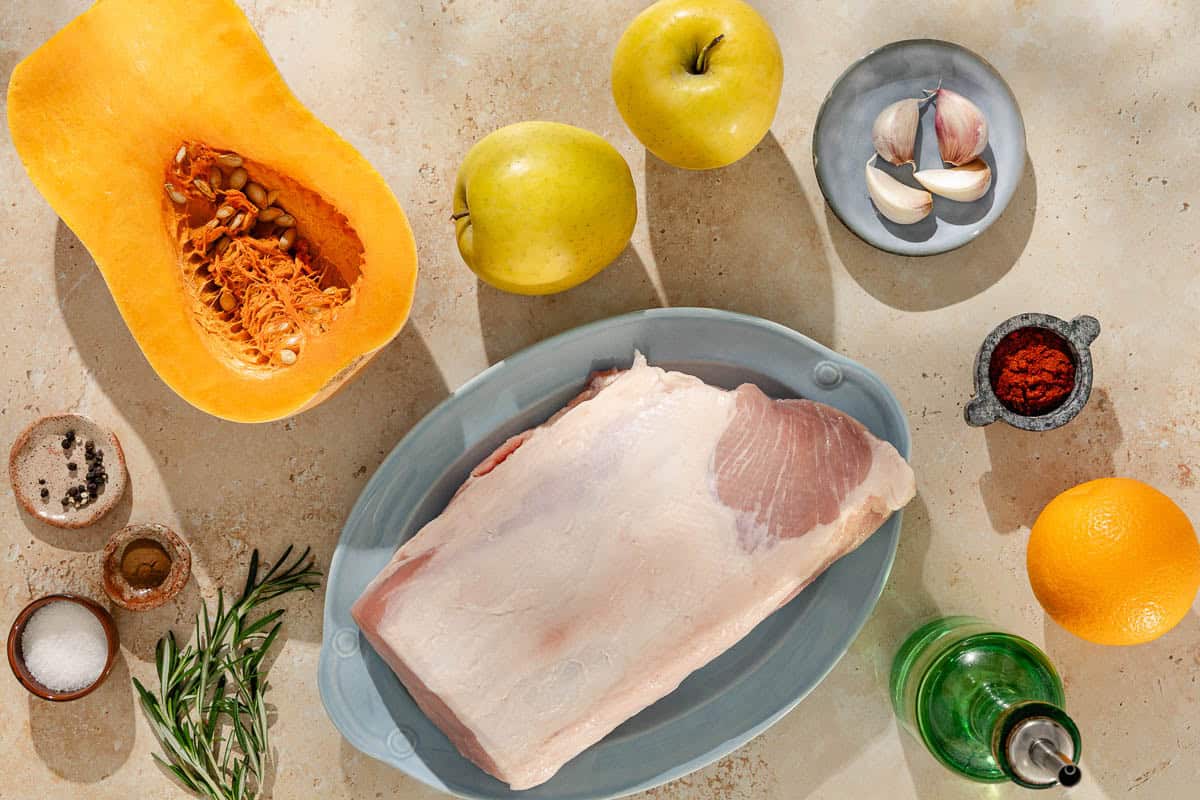 Ingredients for roast pork loin including pork loin, garlic, salt, orange, fresh rosemary, sweet paprika, cinnamon, black pepper, olive oil, butternut squash, and apples.