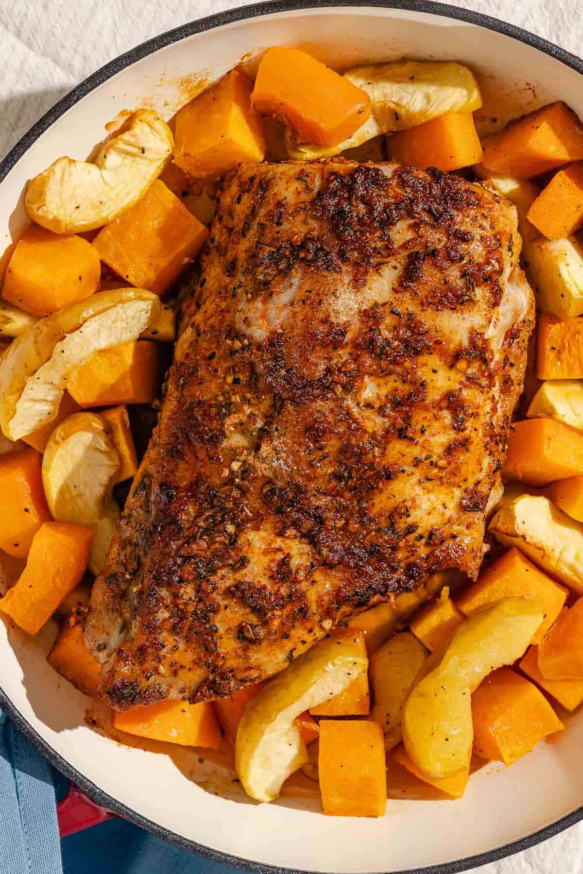 An overhead photo of a roast pork loin with butternut squash and apples in a roasting pan.